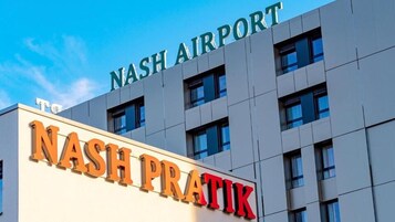 El exterior del edificio del Aeropuerto Nash con el letrero 'NASH AIRPORT' en la parte superior y 'NASH PRATIK' en letras grandes debajo.