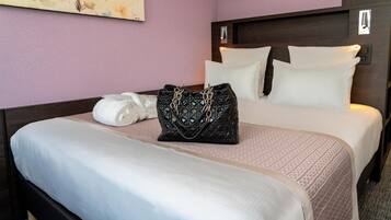 Une chambre d’hôtel avec un lit, des oreillers, une serviette roulée et un sac à main noir posé sur le lit.