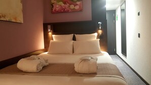 Habitación de hotel con una cama grande, dos lámparas de noche, un cuadro en la pared y una puerta que da a otra habitación.