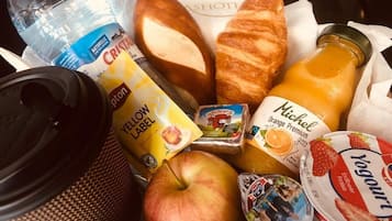 A breakfast basket containing a croissant, apple, juice, yogurt, and a bottle of water.