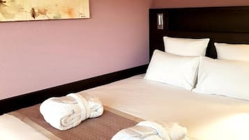 Habitación de hotel con una cama grande, dos almohadas, un cabecero y dos toallas enrolladas sobre la cama.