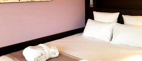 A hotel room with a large bed, two pillows, a headboard, and two rolled towels on the bed.