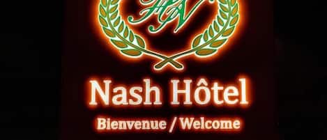A sign for Nash Hotel with a neon 'Nash' logo, welcoming guests and indicating the entrance, reception, and parking areas.