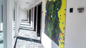 Un pasillo de hotel largo, con puertas y un cuadro grande y colorido en la pared.