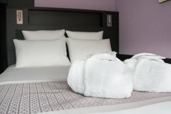 Una cama bien hecha con sábanas blancas y una colcha estampada, junto con dos toallas blancas sobre el suelo.