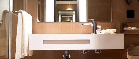 A modern bathroom with a large mirror, a glass shower enclosure, a white sink, and a toilet.