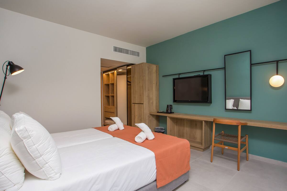 Une chambre d’hôtel moderne équipée d’un lit, d’un bureau, d’une chaise, d’une télévision et d’une armoire.