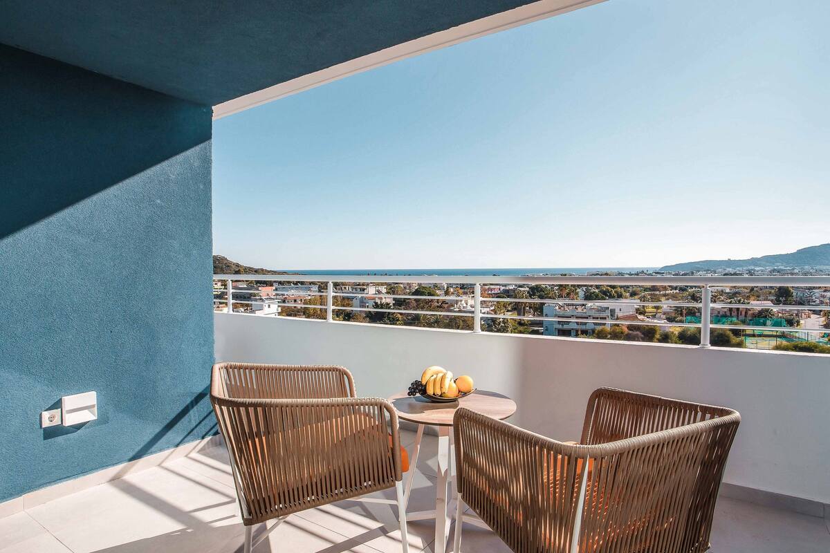Un balcon avec des fauteuils en osier, une table garnie de fruits et une vue sur la ville.