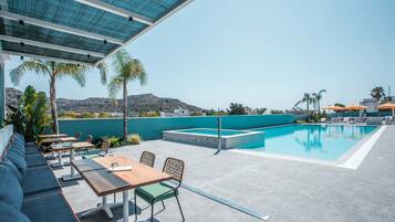 Un área de piscina en la azotea con zona de estar y mesas, rodeada de palmeras y vistas a las colinas.