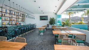 Een moderne bar met een marmeren toonbank, rieten stoelen en uitzicht op het landschap.