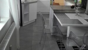 A modern kitchen with white cabinets, a central island, and a dining area with clear chairs. - EverySky Karpacz 3 Maja 66 (Karpacz)
