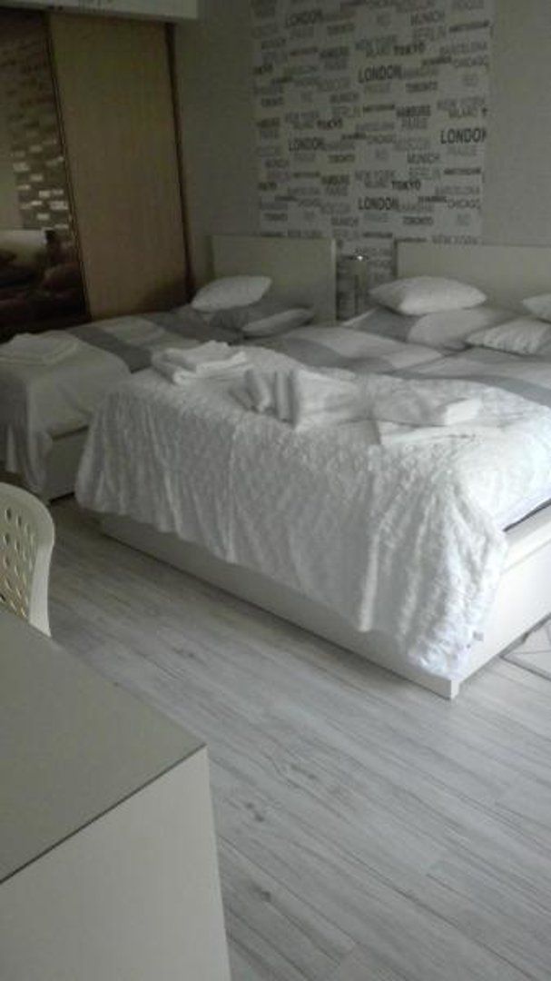 A hotel room with a large bed, a bedside table, and a wall with city names.
