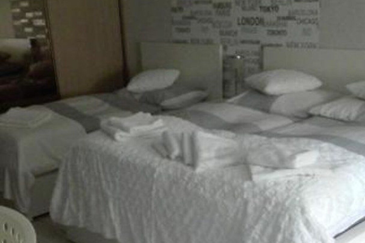 A hotel room with two beds, a wooden wardrobe, and a wall with city names.