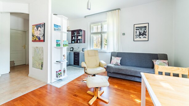 A modern living room with a grey sofa, a white armchair, and a wooden dining table. A kitchen is visible in the background with cabinets and a kettle. - EverySky Karpacz 3 Maja 66 (Karpacz)