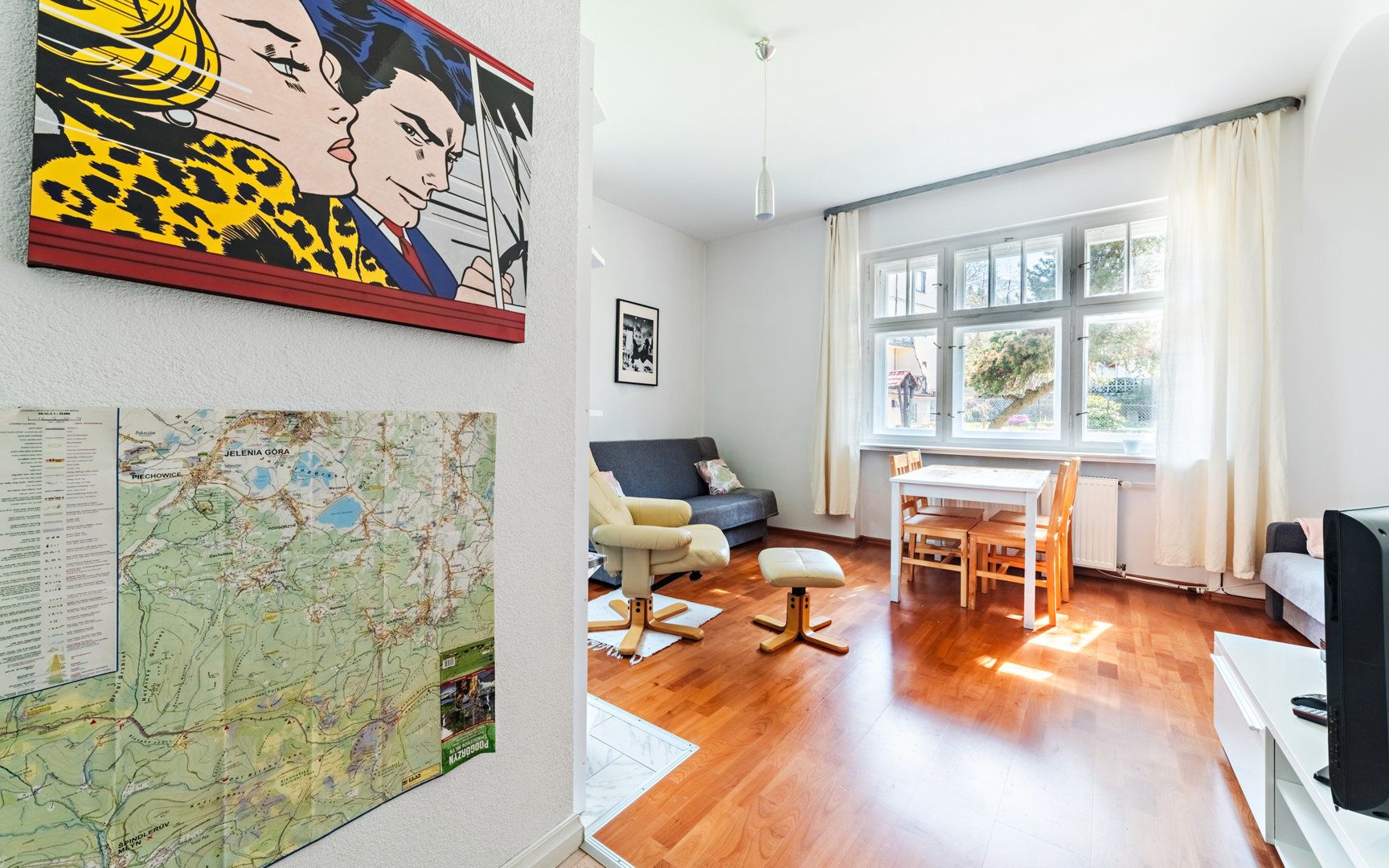 A living room with a map, a sofa, a dining table, and a TV.