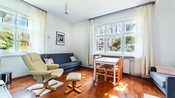 Ein modernes Wohnzimmer mit Sofa, Sessel, Esstisch und Holzboden.