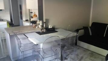 Eine moderne Küche mit einer zentralen Kochinsel, klaren Kunststoffstühlen und einem schwarzen Sofa.