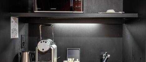 Una kitchenette compacta equipada con microondas, cafetera y máquina de espresso.