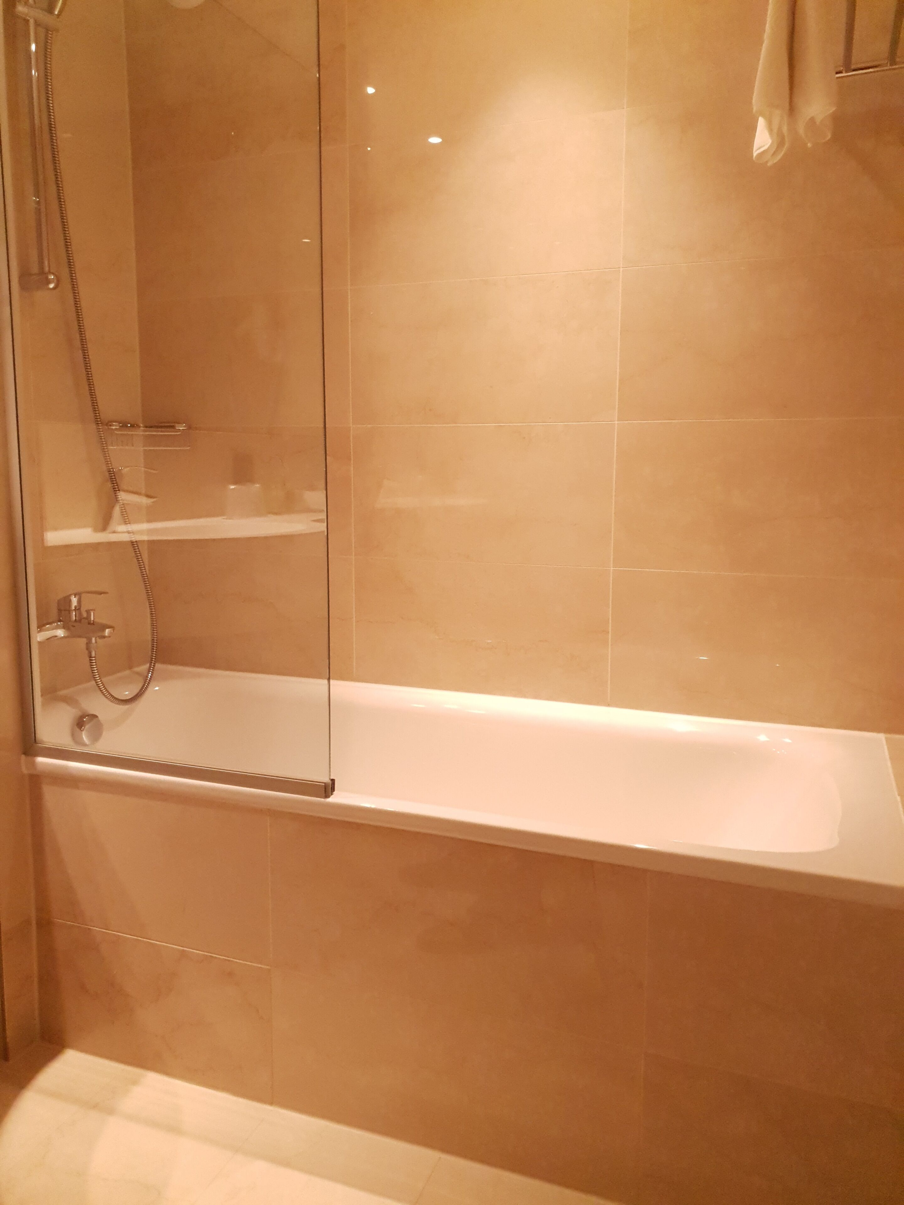Une salle de bain moderne avec une douche à parois de verre, une baignoire blanche et des carreaux de couleur beige.