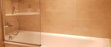 A modern bathroom with a glass-enclosed shower, a white bathtub, and beige tiles.