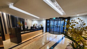 Un vestíbulo de hotel moderno con un mostrador de recepción, un ascensor de vidrio y un suelo de mármol.