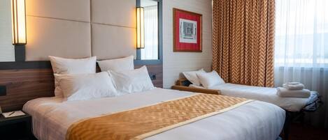 Una habitación de hotel con dos camas, una lámpara grande de pared, un cuadro enmarcado y una ventana con cortinas.
