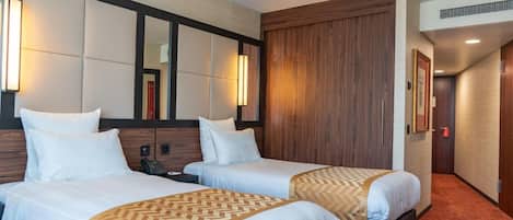 A hotel room with two beds, a wooden wardrobe, a mirror, and a telephone.