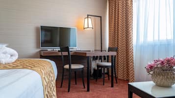 A hotel room with a bed, a desk with a chair, a television, a lamp, and a window with curtains.