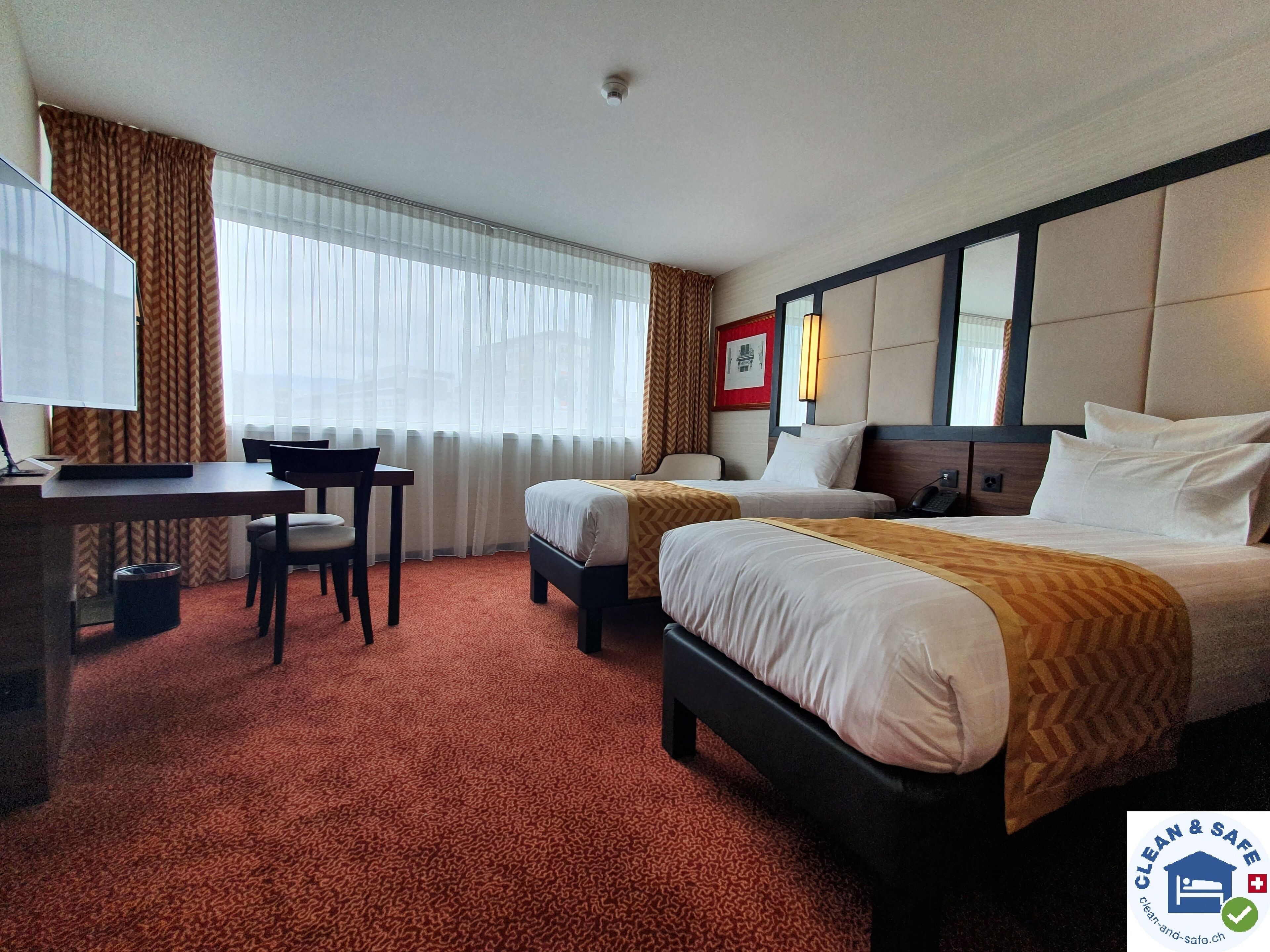 A hotel room with two beds, a desk, and a chair.