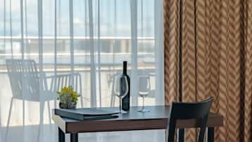 A table with a wine bottle and glass, a small vase with flowers, and a view of the sea through large windows.