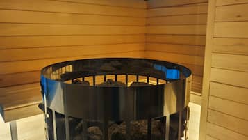 A sauna with a metal grate and rocks inside, surrounded by wooden walls.