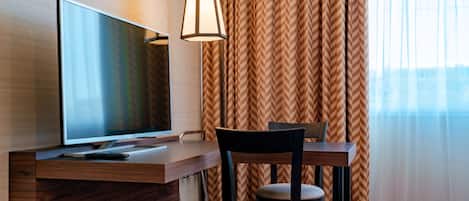 Habitación de hotel con televisor de pantalla plana sobre un escritorio de madera, una lámpara, una silla y una cama.