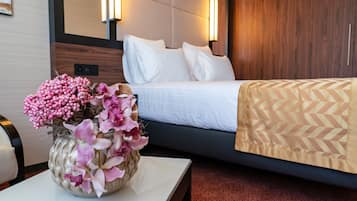 Et hotelværelse med en seng, et natbord med en vase blomster, og en vægmonteret lampe.