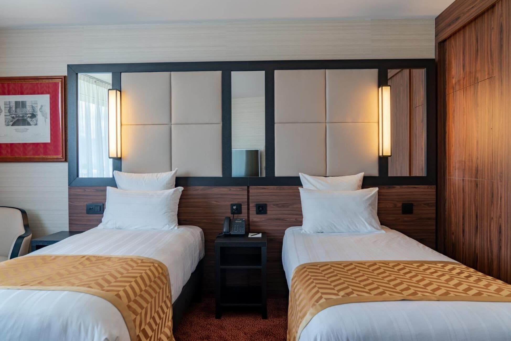 A hotel room with two beds, a small table, a chair, and a framed picture on the wall.