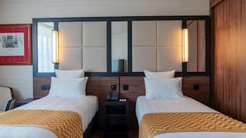 A hotel room with two beds, a small table, a chair, and a framed picture on the wall.