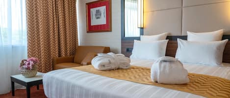 Een hotelkamer met een groot bed, witte kussens, een hoofdbord met een spiegel, een ingelijste foto aan de muur en een bloevas op een nachtkastje.
