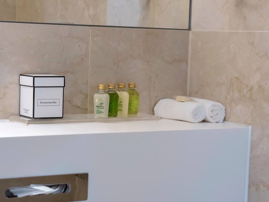 A bathroom counter with a box labeled "Accessories Set," three bottles of liquid, and two rolled towels.
