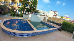 A swimming pool with blue tiles, surrounded by a tiled deck and a building with balconies. - C'est La Vie (Magong)