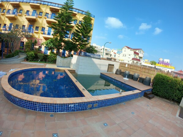 A swimming pool with blue tiles, surrounded by a tiled deck and a building with balconies. - C'est La Vie (Magong)