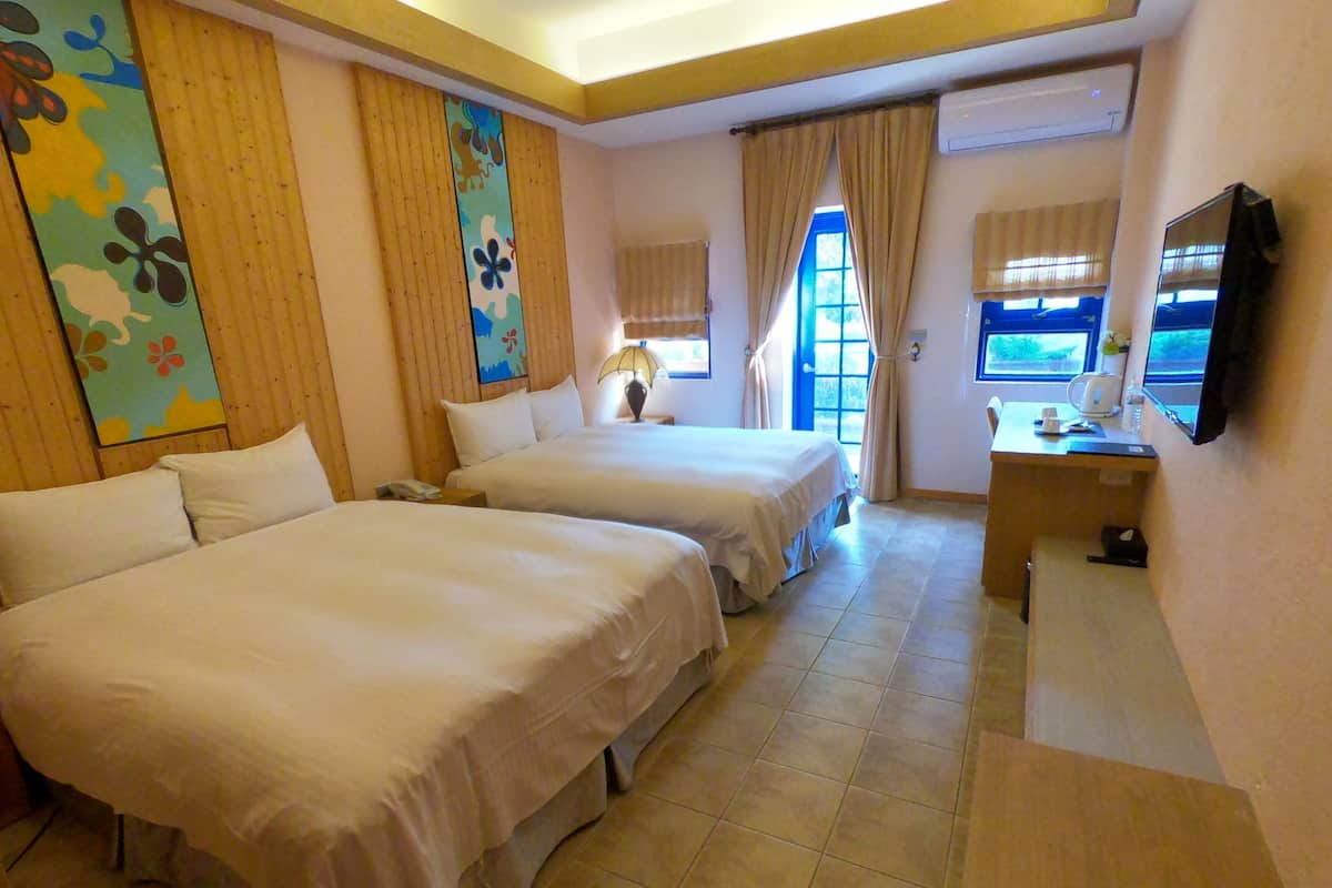 A hotel room with two beds, a desk, a TV, and a window with curtains.