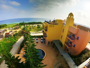 Um edifício amarelo com piscina e área externa para sentar, com vista para uma praia.
