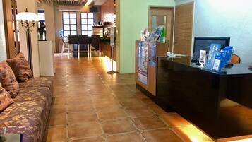 A hotel lobby with a reception desk, a sofa with floral upholstery, and a tiled floor.