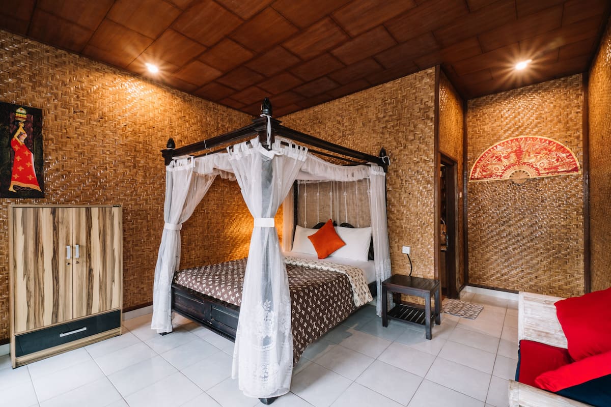 Une chambre à coucher avec un lit à baldaquin, une armoire, une petite table et un canapé rouge.
