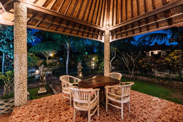 An outdoor seating area with a thatched roof, stone pillars, and a tiled floor.