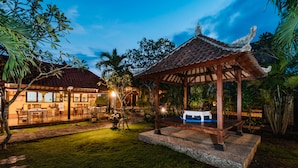 A traditional-style gazebo with a tiled roof, surrounded by a well-maintained garden with palm trees and a patio area with outdoor seating. - Bunda 7 Bungalow (Lembongan Island)