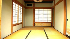 Een traditionele Japanse kamer met tatami vloerbedekking, schuifdeuren van shoji-papier en een houten plafond met een hanglamp.