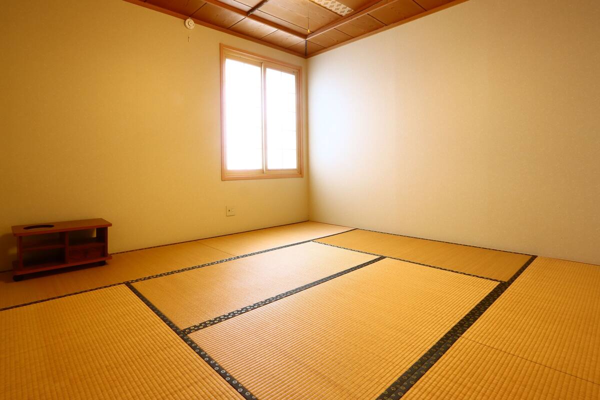Een kamer met tatami vloerbedekking, een raam en een klein houten plankje.