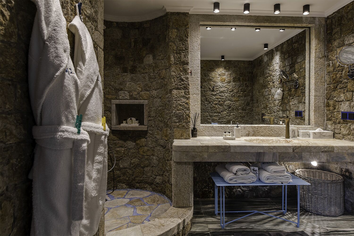 A bathroom with a stone wall, a large mirror, a sink, and a towel rack.