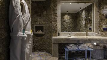 A bathroom with a stone wall, a large mirror, a sink, and a towel rack.