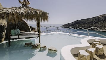 Una piscina infinita con un área de estar cubierta por un techo de paja y vistas al mar.
